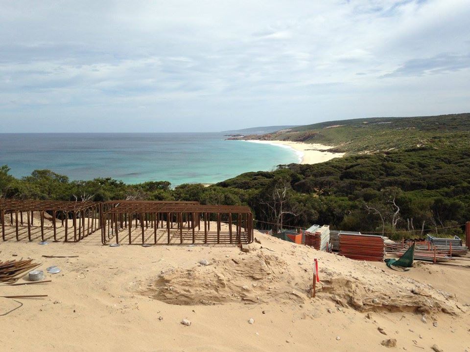 Sandy coastal construction site with steel rebar frames and stacked materials overlooking the ocean