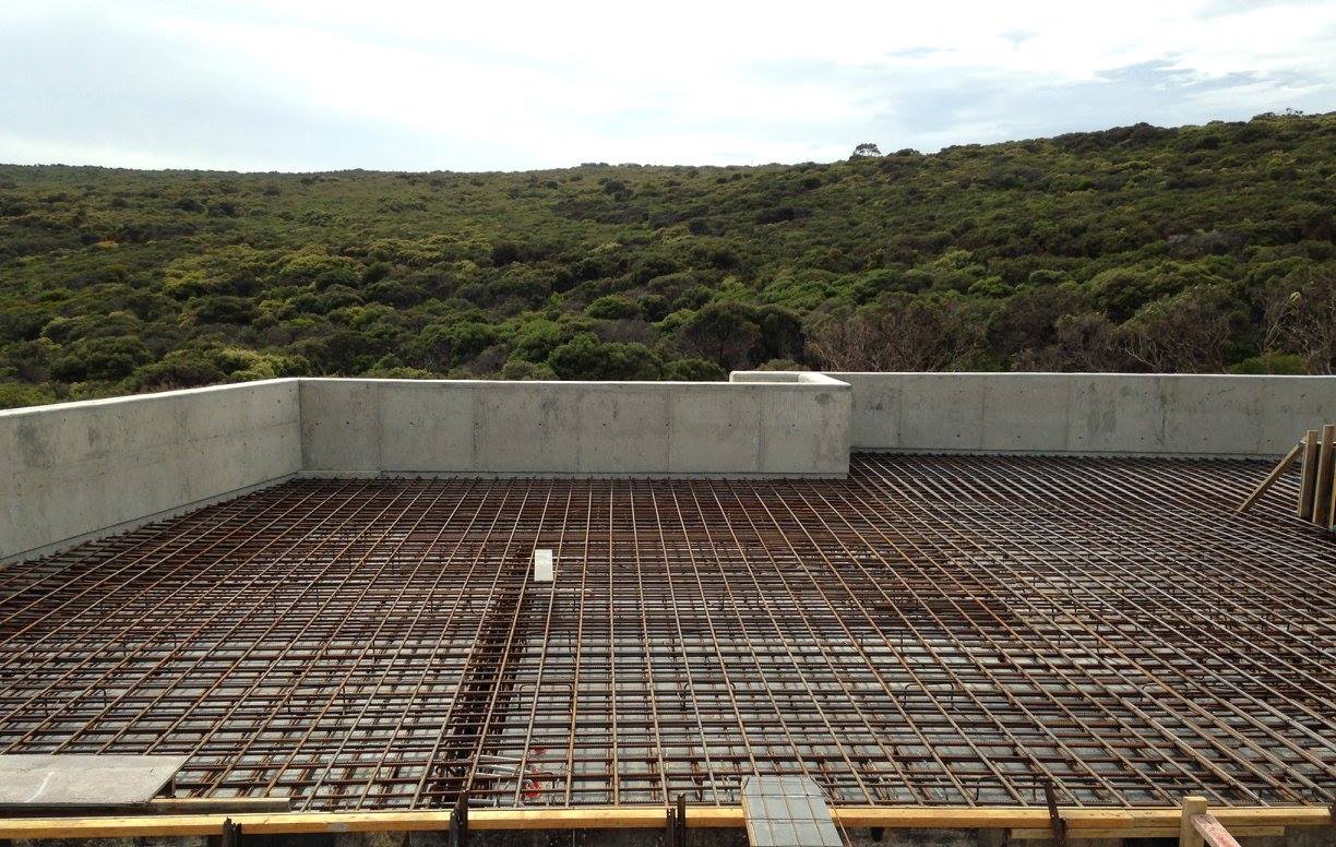 Dense steel rebar grid prepared for a concrete slab with wooden formwork and a forested hillside beyond