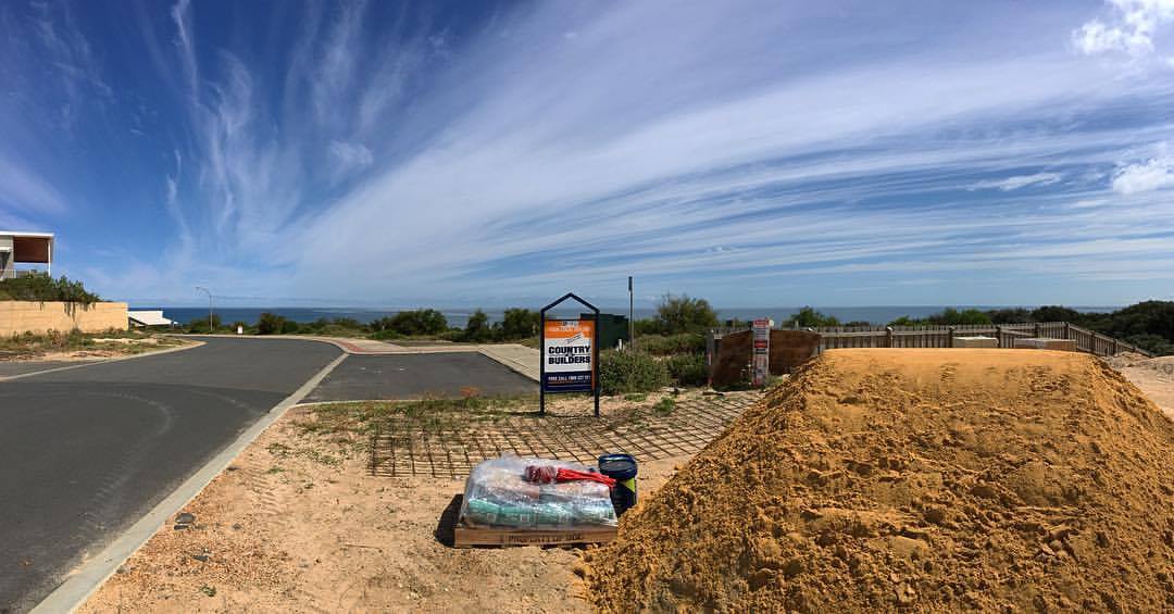 Coastal construction site with a large sand pile, wrapped materials and reinforcing mesh under a blue sky